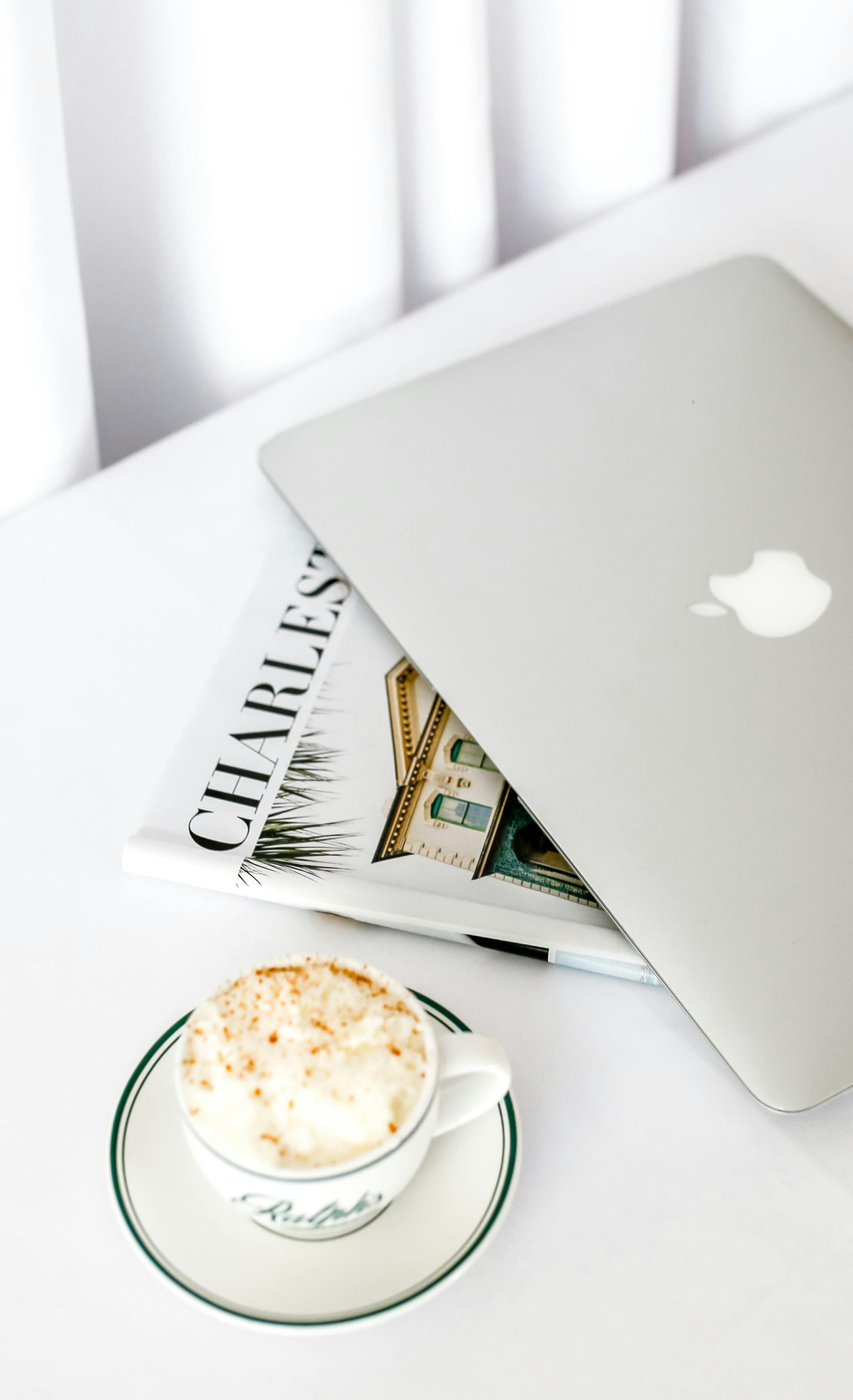 A silver laptop, magazine, and cappuccino on a white table hint at a smooth Squarespace website design process.